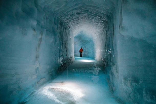 Person walking through long ice cave  